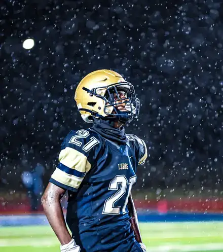 Football player number 21 in a navy uniform and gold helmet standing in the rain