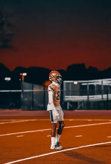Football athlete in an orange uniform beneath a deep red evening sky