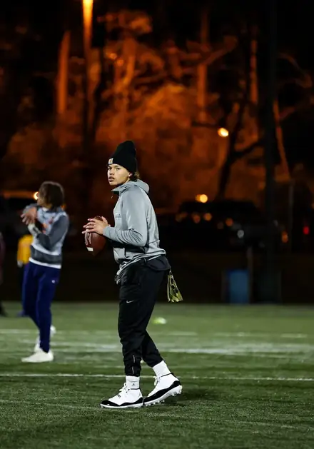 Football athlete in a gray top holding a ball at night