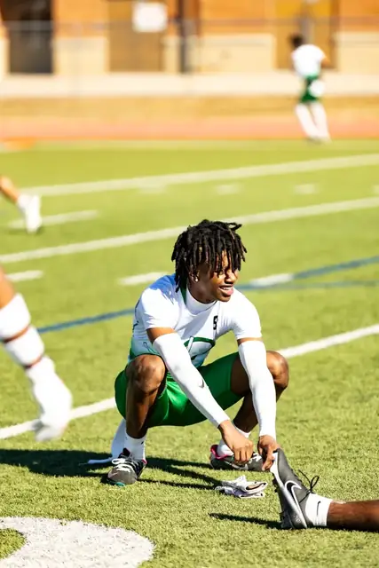 Athlete in a white shirt stretching on a sunny football field