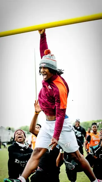 Athlete in maroon and orange celebrating beneath a yellow goalpost with teammates